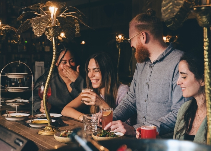 Eine Gruppe von Freunden, die in einer lebhaften Bar lachen und mit ihren Getränken anstoßen.